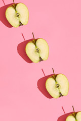 Colorful fruit pattern of fresh cutted apple halves with pits on coral pink background, top view