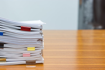 Close up pile of unfinished paperwork on office desk waiting to be managed and inspected. Stack of homework assignment with colorful paper clips. Report papers stacks. Business and education concept.