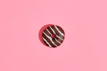 Food design. Close up high quality image of chocolate glazed donut with white strips on coral pink background