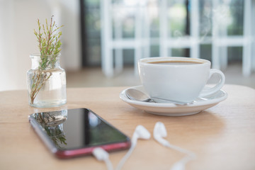 white cup of coffee and blur smartphone on wood table