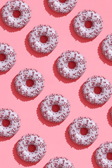 Food design with tasty pink glazed donut on coral pink pastel background top view pattern