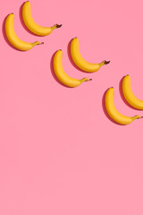 Obraz na płótnie Canvas Pattern composition of a pair of bananas lying next to a pink background , top view