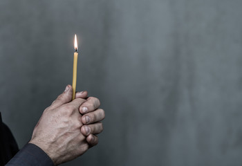 Closeup old mans hands hold a candleon dark background. Space for text