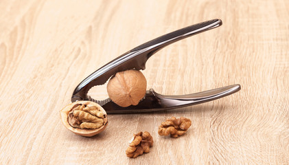 Chrome nutcracker and walnuts lie on a wooden table. Kernels of nuts and halves