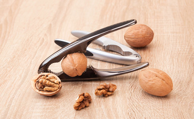 Two chrome nutcrackers and walnuts lie on a wooden table. Kernels of nuts and halves