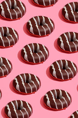 Food design with tasty chocolate glazed donut with white strips on coral pink pastel background top view pattern