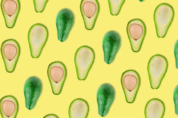 Scattered whole and halves of organic avocado with and without kernels on yellow table in kitchen or market. Top view. Cooking concept