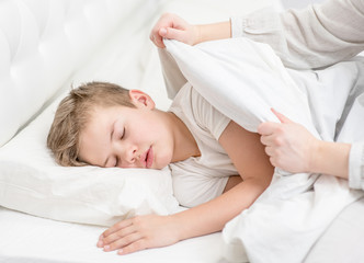 Obraz na płótnie Canvas Mom covering young sleeping boy with blanket