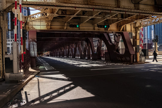 Pedestrian walks alongside el tracks as they cast shadow patterns onto Wells Street