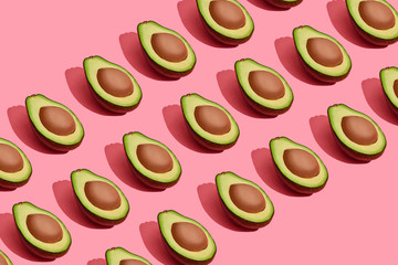 Colorful fruit pattern of fresh cutted avocado halves with pits on coral pink background, top view