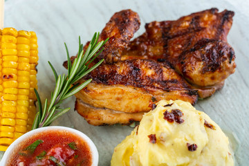 The chicken on a grill with potatoes and hot sauce, is served with corn on a grill