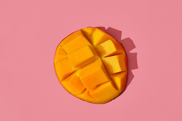 Colorful fruit pattern of fresh juicy cutted mango laying on the middle of the image on coral pink...