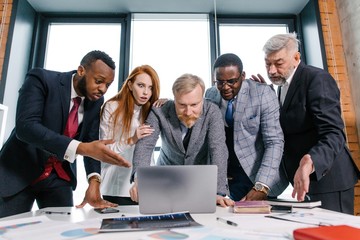 Corporate business team working in the office space standing at the table looking in surprise at the laptop monitor