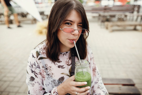 Stylish Hipster Boho Girl Drinking Spinach Smoothie In Glass Jar With Metal Reusable Straw At Street Food Festival. Happy Woman In Sunglasses With Healthy Drink In Summer Street. Zero Waste