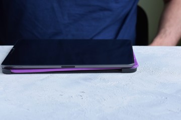 Blurred caucasian man puts on a new purple leather case on tablet with selective focus. White male hands are holding a tablet and putting on a violet cover. Man using a digital tablet