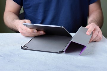 Blurred caucasian man puts on a new purple leather case on tablet with selective focus. White male...