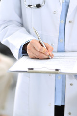Doctor woman filling up medical form while standing near reception desk at clinic or emergency hospital.Unknown physician at work, hands close-up. Medicine and healthcare concept