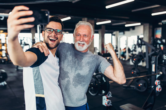 .Senior man taking selfie photo with his personal trainer while exercising at gym.