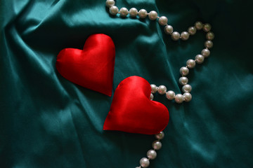 two red silk hearts made of fabric on a contrasting background and pearls