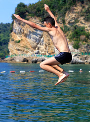 Brave teen jump in the sea against the backdrop of rocks and shoreline