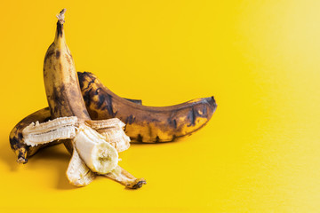 Two overripe blackened ugly bananas on bright yellow background .