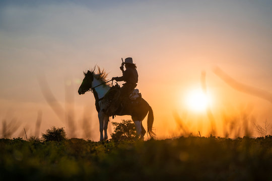 silhouette cowboy fire a gun on a horse back in sunset