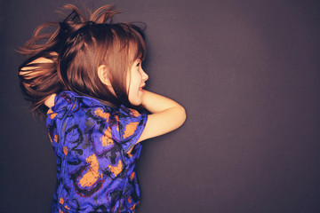 Charismatic girl in a blue dress with abstract orange flowers on a dark background. Place for inscription. child
