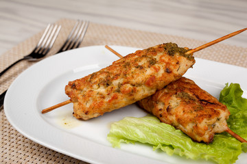 Meat kebab on wooden skewers with a leaf of green lettuce.