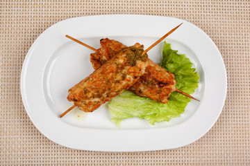 Meat kebab on wooden skewers with a leaf of green lettuce.