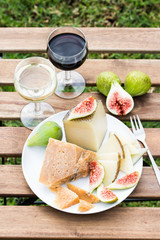 Cheese, figs and glasses of red and white wine on a wooden table.