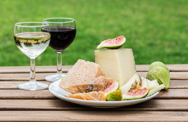 Cheese, figs and glasses of red and white wine on a wooden table.
