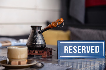 Closeup traditional Turkish coffee in cezve on wooden stand, porcelain cup with refined sugar cubes served on table in restaurant. Сoncept breakfast in restaurant at luxury hotel
