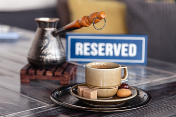 Closeup traditional Turkish coffee in cezve on wooden stand, porcelain cup with refined sugar cubes served on table in restaurant. Сoncept breakfast in restaurant at luxury hotel