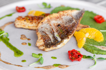 Closeup fried sea bass fillet with green pea puree, tomatoes, sauce, orange slices. Concept professional photography, photosession new menu, profession food stylist, flat-lay, freelancer