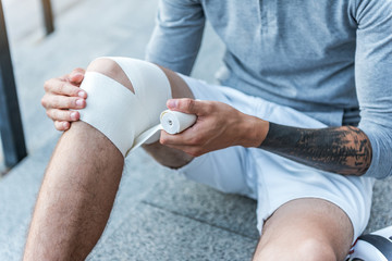 Tattooed man sitting and using elastic bandage