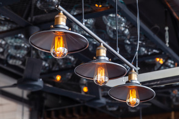 Black iron loft chandeliers with edison lamps on a black background, bokeh. Concept of modern...