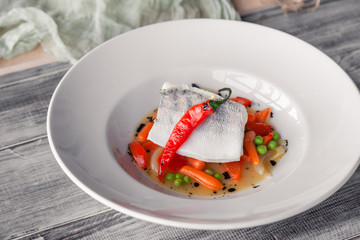 Closeup fillet stewed pike perch with vegetables, chilli pepper, tomato, onion, mini carrot with sauce served on table in restaurant. Concept professional food shooting, photo session of new menu