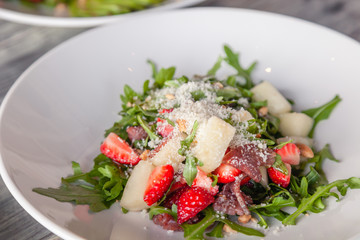 Close-up fresh summer salad with basturma jerky, greens, arugula, strawberries, melon, parmesan cheese. Concept delicacy, new menu in trendy restaurant