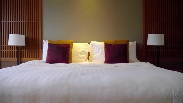 zoom out steady shot of a king queen size double bed indoor hotel room, moody electric light decorated white red bed freshly made bed sheets light brown back wall