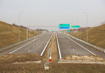 Unfinished two-lane highway with signposting signs. New road without cars. The development of transport infrastructure. Landscape design of the ring road of the metropolis