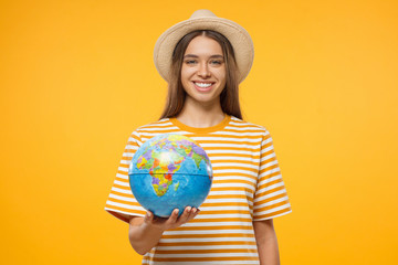 Travel concept. Young woman tourist holding globe with one hand, isolated on yellow background