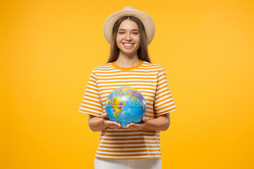 Travel concept. Young female tourist holding globe with both hands, isolated on yellow background