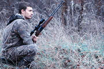 A man in camouflage and with a hunting rifle in a forest on a spring hunt