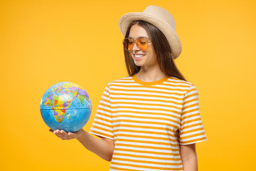 Travelling concept. Young teen tourist holding globe with one hand, isolated on yellow background