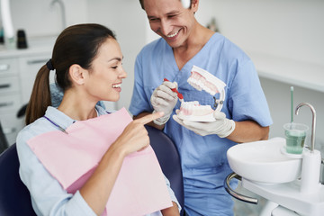Charming lady looking at teeth model in dentist hand and pointing at it