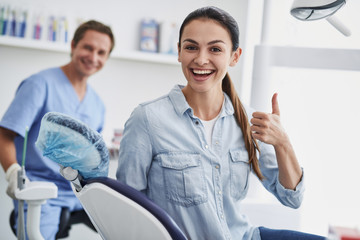 Lovely young lady doing thumbs up sign at modern dental office