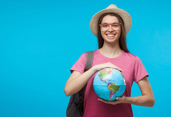 Smiling girl holding globe with both hands, isolated on blue background