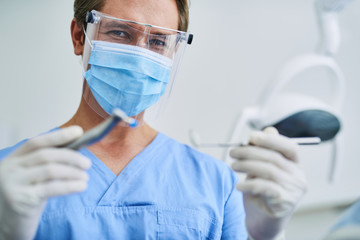 Male dentist in protective mask demonstrating dental tools