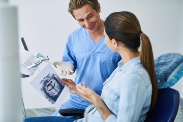 Friendly dentist explaining results of orthopantomogram to young lady