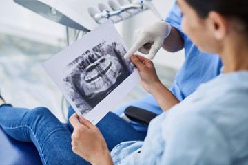 Young lady looking at dental x-ray while dentist pointing at it - obrazy, fototapety, plakaty